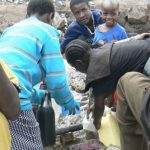 Women (bending over) collecting water from a common faucet while