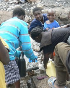 Women (bending over) collecting water from a common faucet while