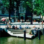 Amsterdam city with people resting and sitting by the water.
