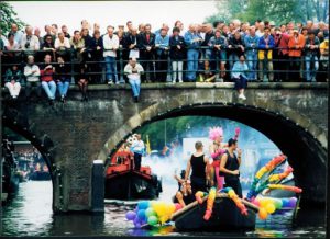 Boat passing under a bridge while people watch from above.