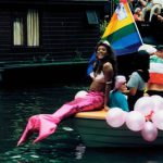 Gay pride mermaid resting on the edge of a boat.