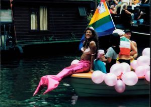 Gay pride mermaid resting on the edge of a boat.