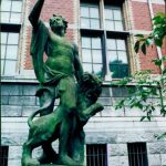 A statue standing tall in front of a brick building.