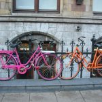 Two bicycles parked up on a curb against a fence.