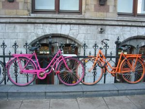 Two bicycles parked up on a curb against a fence.