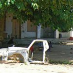 A stripped truck frame in the front yard of a