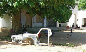 A stripped truck frame in the front yard of a