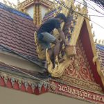 Painter touching up gold-colored details on a temple entry gate--bare