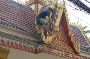 Painter touching up gold-colored details on a temple entry gate--bare