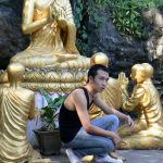 Young modern Lao guy among old Buddhist statues