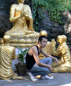 Young modern Lao guy among old Buddhist statues