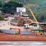 Huge tree stumps being loaded onto a cargo boat; the