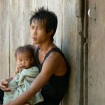 Father and infant watching tourists walk through his village; what