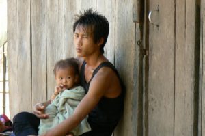 Father and infant watching tourists walk through his village; what