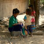 Mother peeling potatoes as kids watch and her piglet wanders