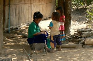 Mother peeling potatoes as kids watch and her piglet wanders