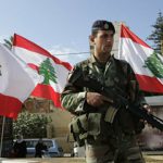 A Lebanese army soldier, stands next to Lebanese flags as