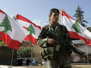 A Lebanese army soldier, stands next to Lebanese flags as