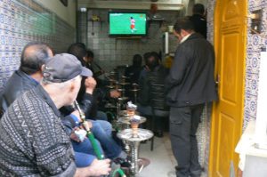 Men dressed in usual dark clothes smoking tobaccothrough hookas (water