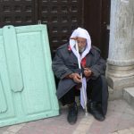 Old man resting next to an ancient column and a