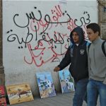 Two students in central Tunis walking past graffiti wall slogans.