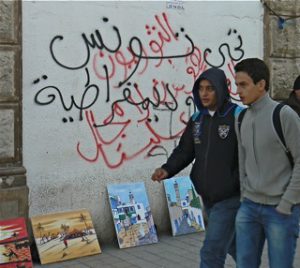 Two students in central Tunis walking past graffiti wall slogans.
