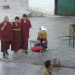 Tibet, Lhasa: three monks walk across Barkhor Square. Monks' salaries are