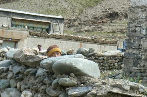 Tibet: child hiding behind stone wall of his house.