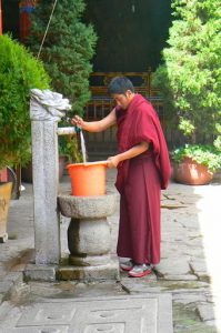 Tibet: Lhasa Young monk drawing well water at Jokhang Temple.