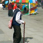 Tibet: Lhasa Elderly pilgrim passing prayer flags by Jokhang.