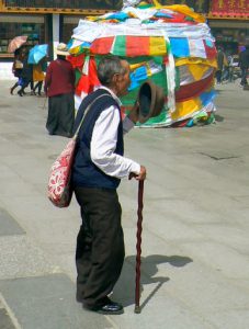 Tibet: Lhasa Elderly pilgrim passing prayer flags by Jokhang.