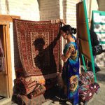 Uzbekistan: Bukhara Sayfiddin carpet shop with saleswoman in pretty silk dress.