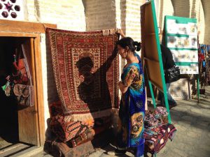 Uzbekistan: Bukhara Sayfiddin carpet shop with saleswoman in pretty silk dress.